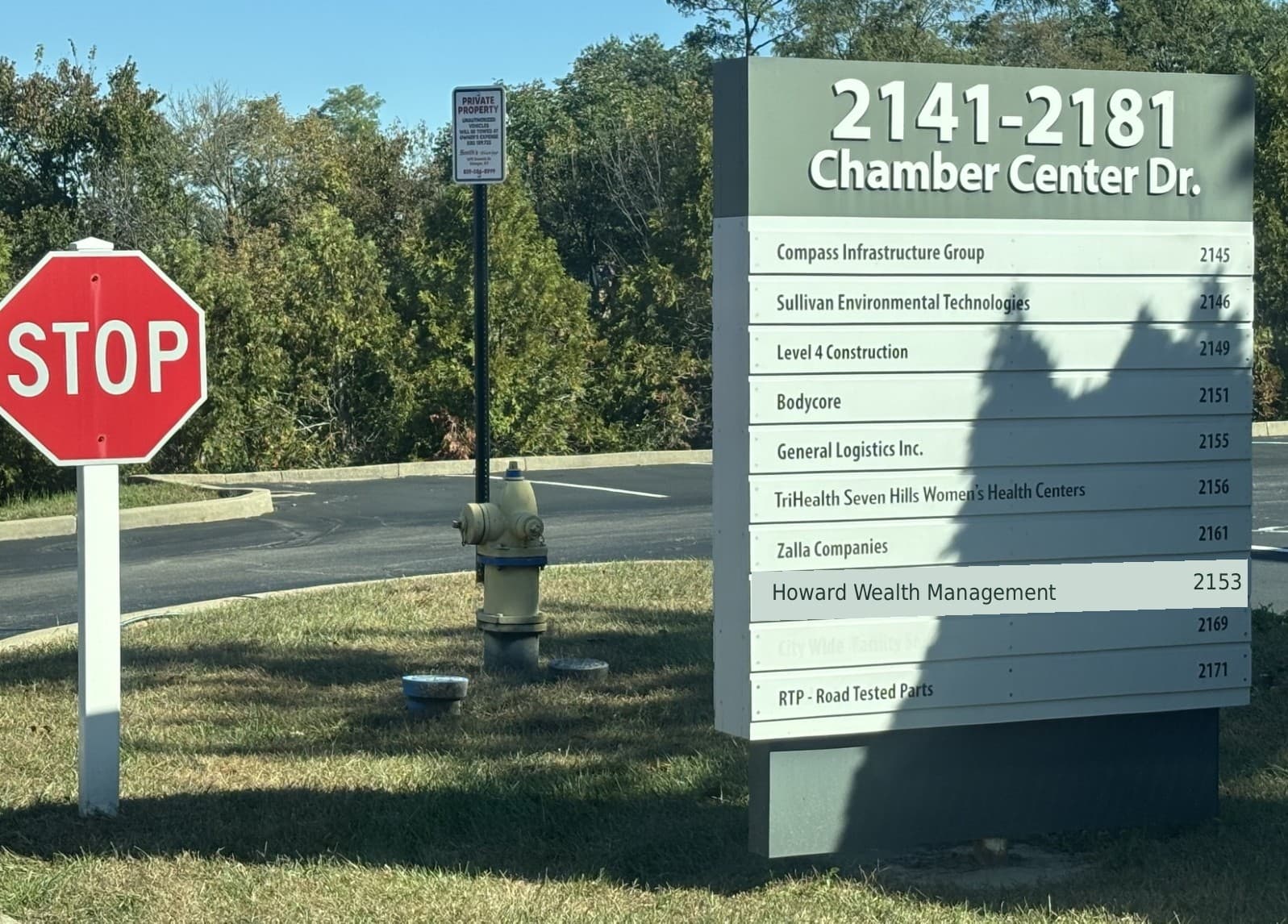 Stop sign beside the directory for 2141–2181 Chamber Center Drive, listing Howard Wealth Management at 2153.
